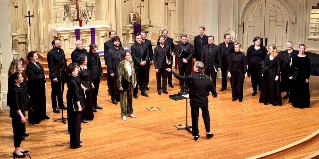 Vox Humana chorus on-stage. Adults singers dressed in black.